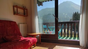 A room with a red sofa, a small wooden table, and a balcony with blue chairs.