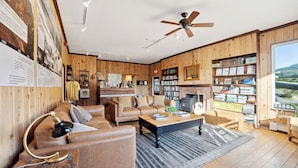 A cozy living room with a fireplace, leather sofas, a coffee table, and a bookshelf filled with books.