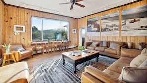 A spacious living room with wooden walls, a large window, and a ceiling fan.