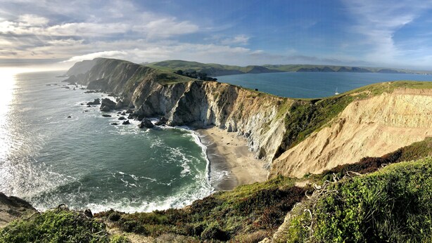 A coastal landscape with cliffs, a beach, and a view of the ocean.