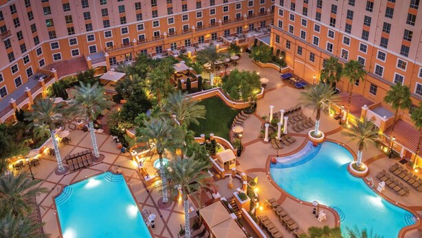 Ein Hotel mit mehreren Schwimmbecken, Außenbereichen zum Sitzen und Palmen.