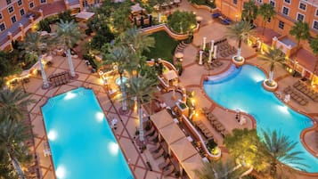 A hotel with multiple swimming pools, outdoor seating areas, and palm trees.