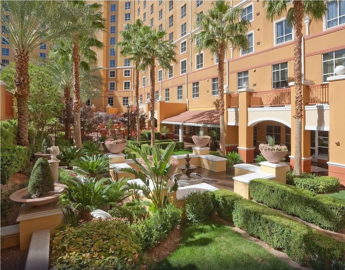 A courtyard with palm trees, a fountain, and a building with balconies.