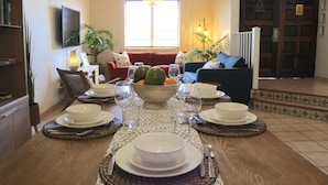 A dining table set with white plates, bowls, and glasses, surrounded by chairs. - Seaside, Tennis, Pickleball, Golf, Pool (Humacao)