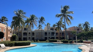 A swimming pool with lounge chairs, palm trees, and a building with balconies in the background. - Seaside, Tennis, Pickleball, Golf, Pool (Humacao)
