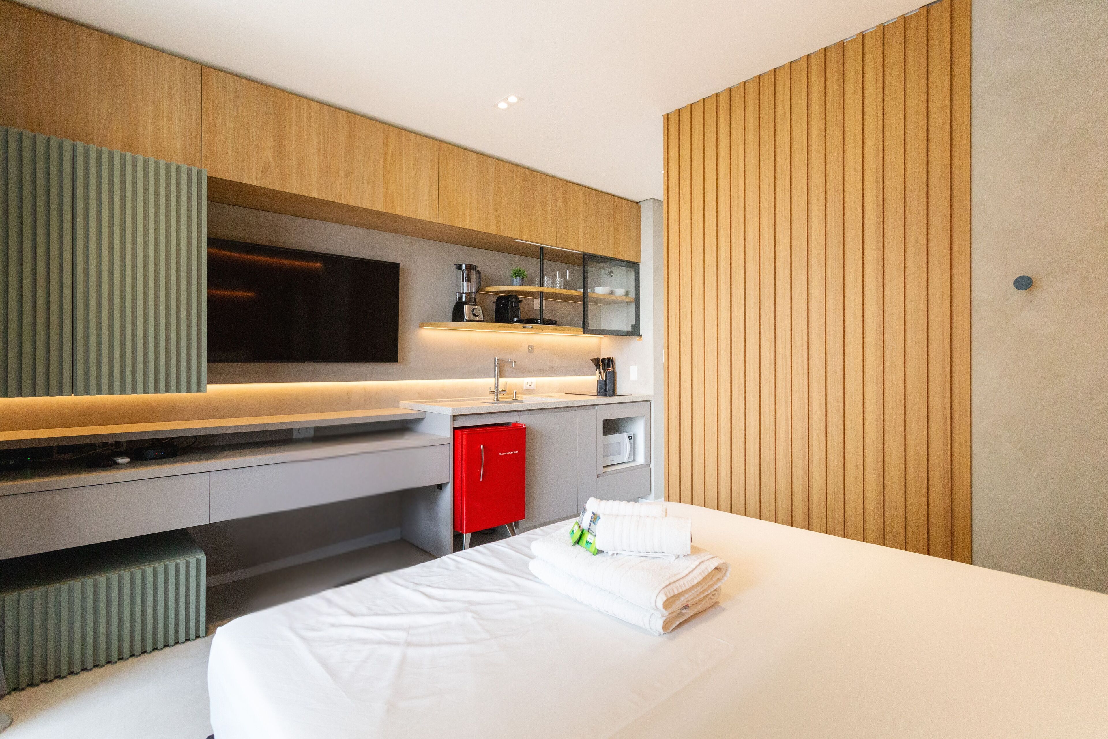 Et moderne hotelværelse med en seng, et lille tekøkken, en rød minibar og et fjernsyn.
