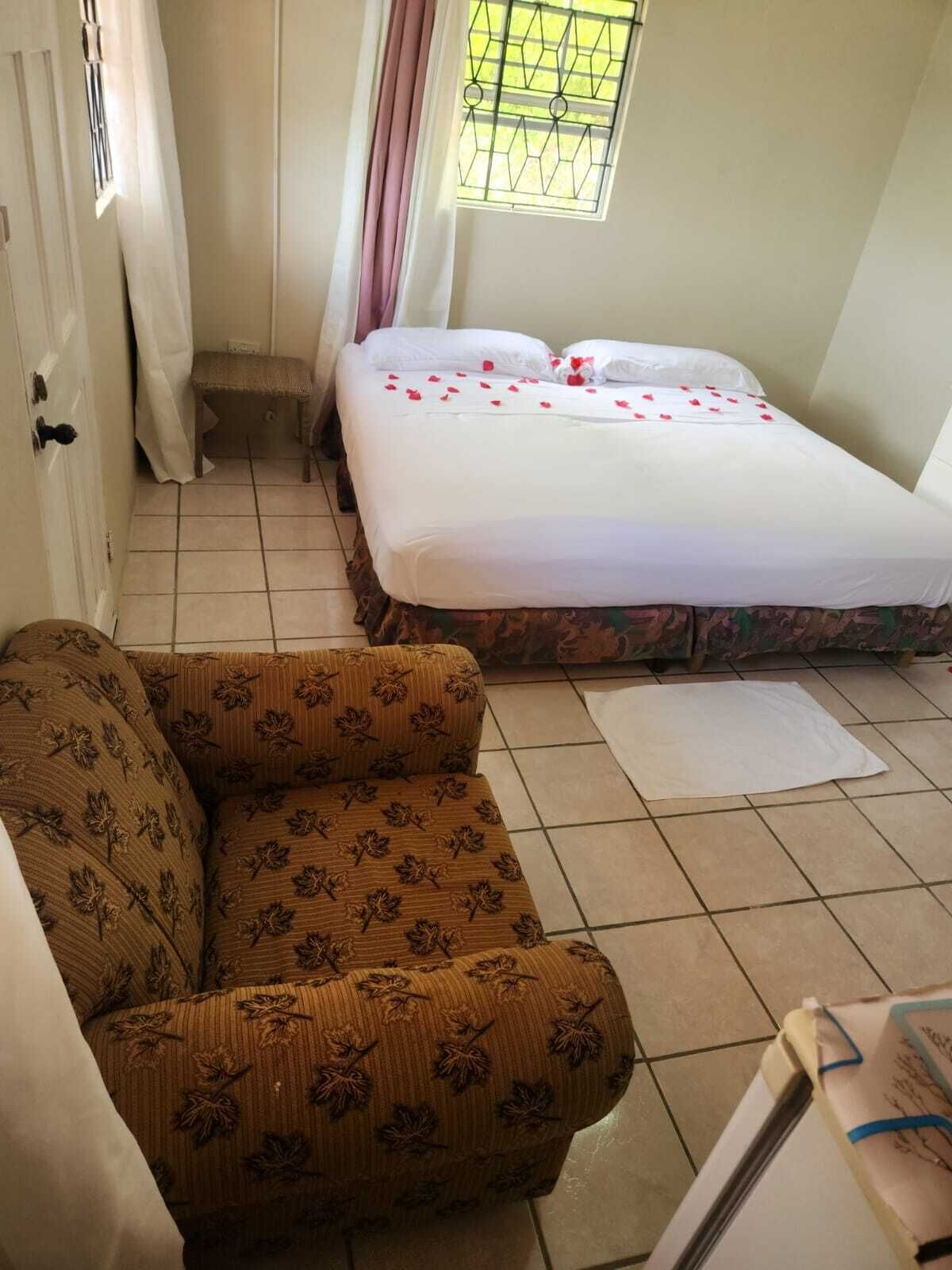 A room with a bed, a sofa, a window with a metal grill, and a door.