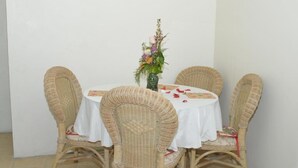 A round table with a white tablecloth, surrounded by wicker chairs. A vase with flowers is placed in the center of the table. - Hilltop View Guesthouse (Castries)