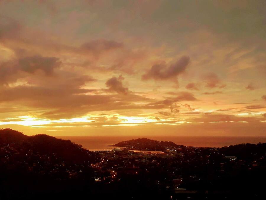 Een zonsondergang boven een stadsgezicht, met gebouwen die als silhouetten tegen de lucht staan.