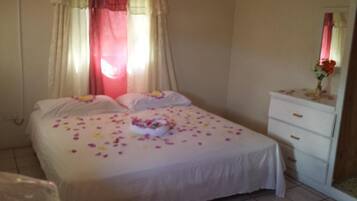 A neatly made bed with a white bedspread and pillows, a bedside table with a vase of flowers, and a mirror above it.