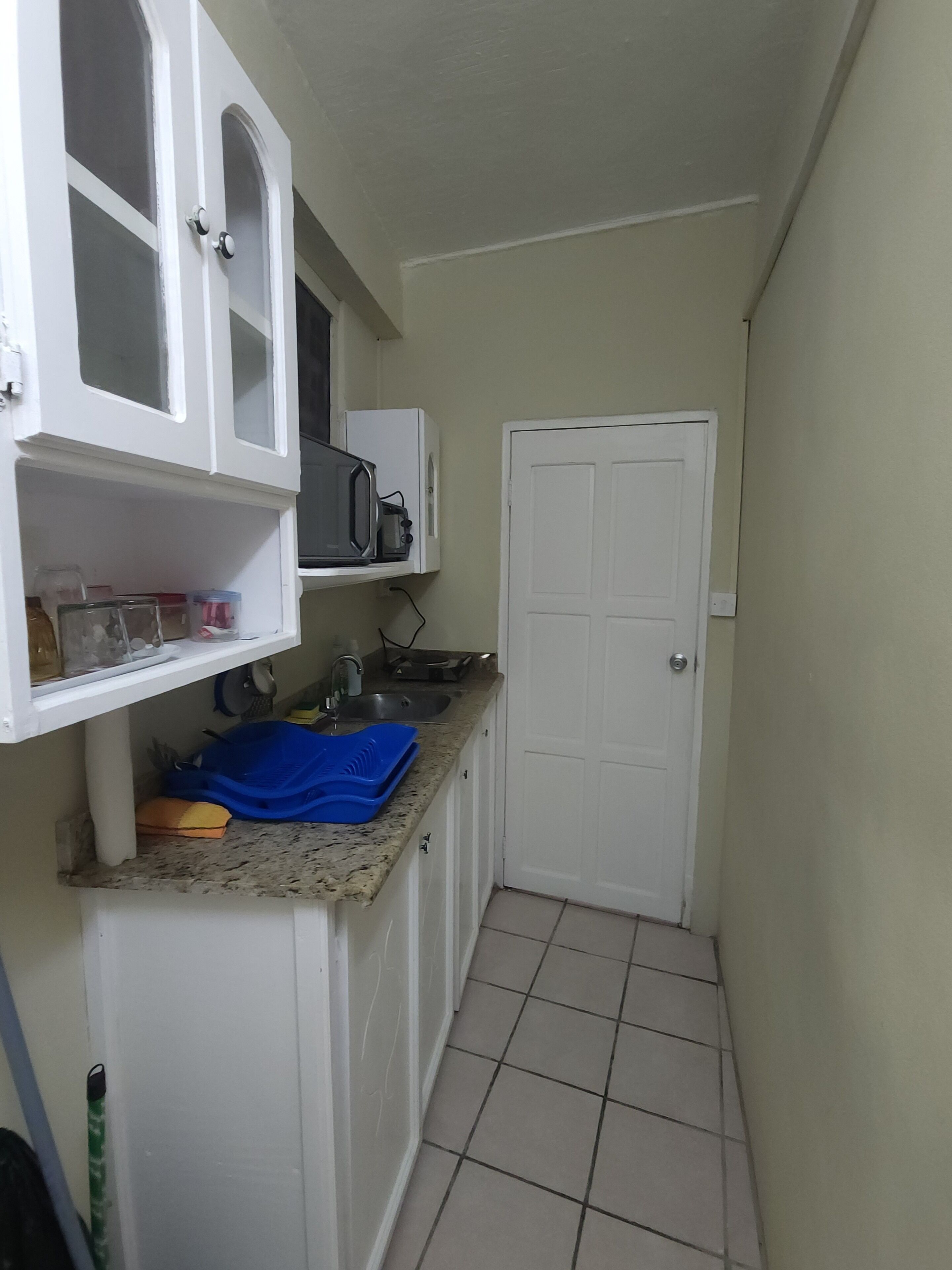 Una cocina estrecha con gabinetes blancos, un microondas y un lavamanos.