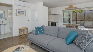 Una sala de estar moderna con un sofá gris, una mesa de centro redonda y una mesita auxiliar de mimbre.