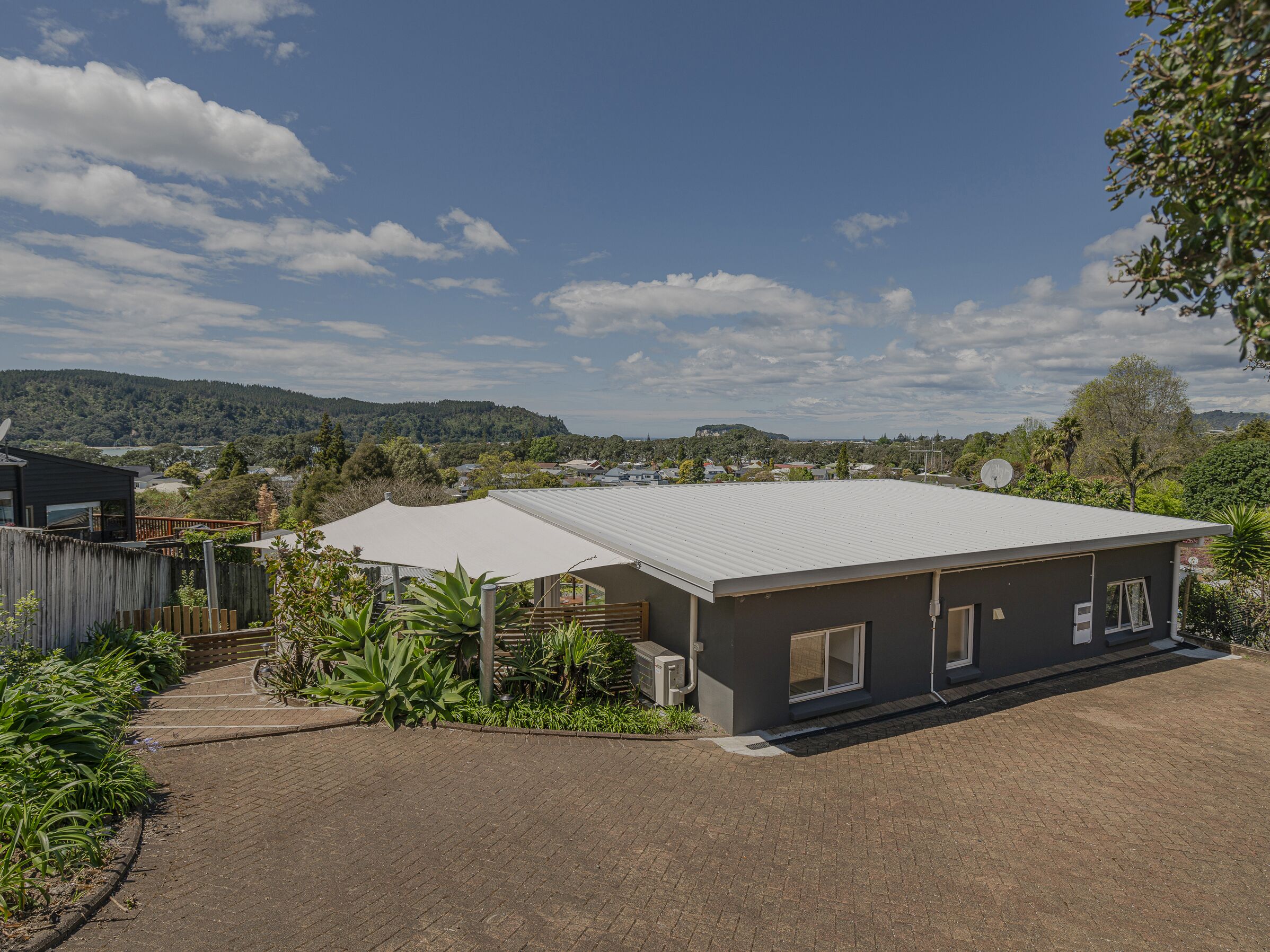 A modern house with a flat roof, surrounded by a garden and a paved driveway.