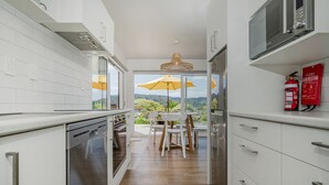 Una cocina moderna con armarios blancos, electrodomésticos de acero inoxidable y vistas a un paisaje exuberante a través de amplias ventanas.