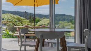 Un comedor con mesa y sillas, una sombrilla amarilla y vistas a zonas verdes y colinas.