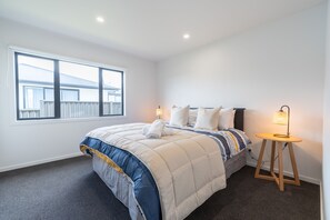 Et soveværelse med en stor seng, et natbord med lampe og et vindue med udsigt til en bygning.