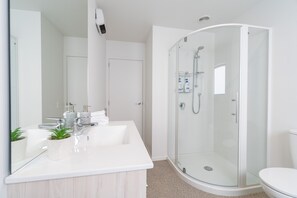 Et moderne badeværelse med en brusekabine i glas, en hvid vask med spejl og et toilet.