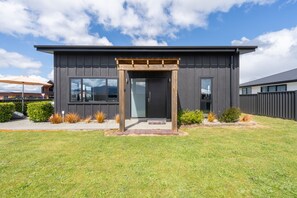 Et moderne hus med mørk facade, en overdækket træindgang og en velplejet græsplæne.