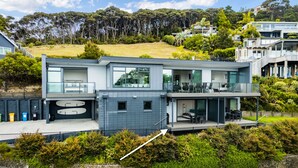 Una casa moderna de dos pisos con balcón, garaje y vistas del entorno verde y las colinas.