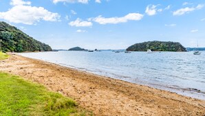 Una playa con barcos en el agua y colinas al fondo.