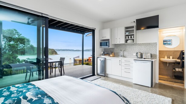 Un dormitorio moderno con una cama grande, un balcón con vistas al mar y una cocina con armarios blancos y un televisor de pantalla plana.