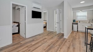 Een modern appartement met houten vloeren, witte muren, een keuken met raam en een slaapkamer met televisie.