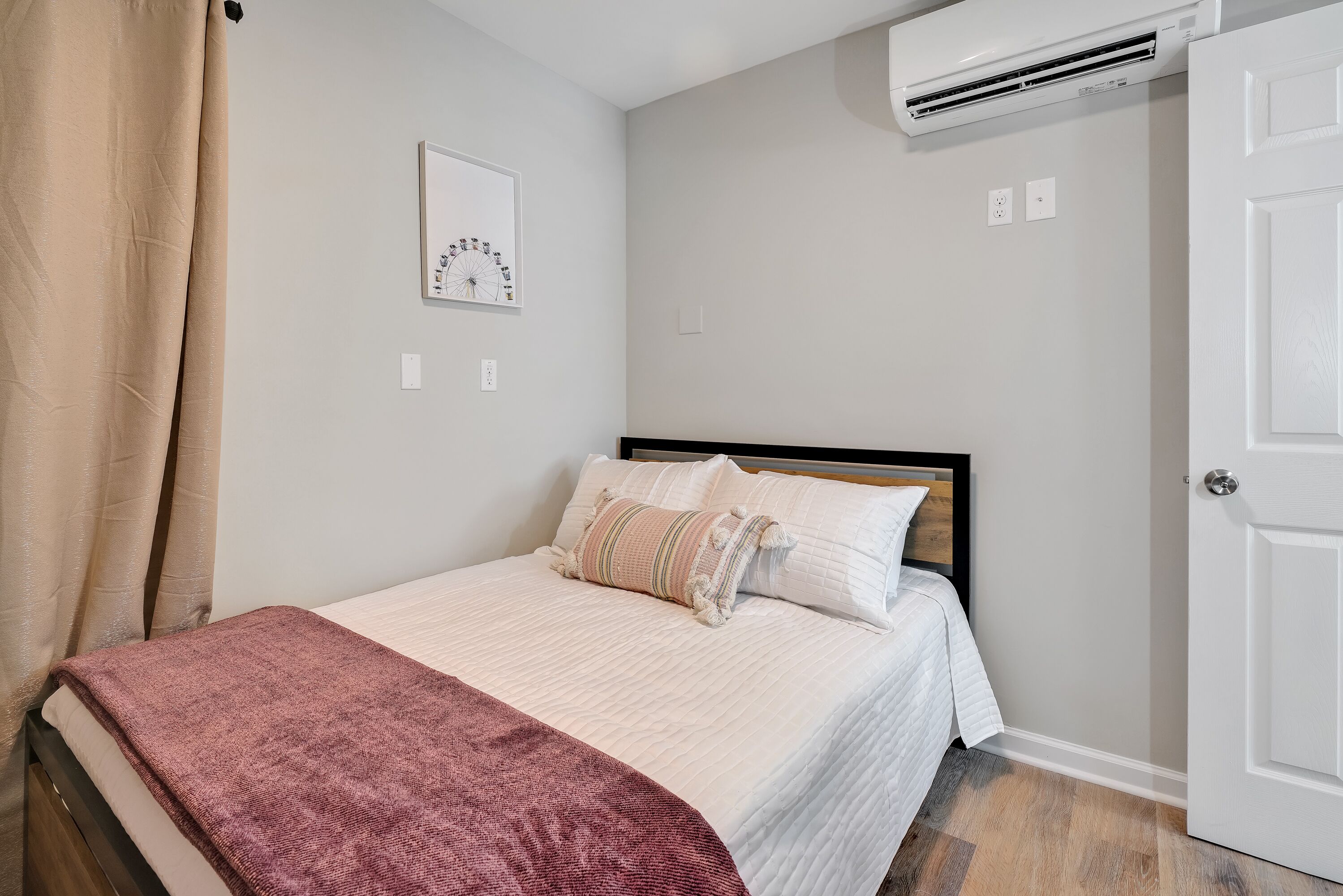 Un dormitorio con cama, aire acondicionado de pared, una puerta y un cuadro en la pared.