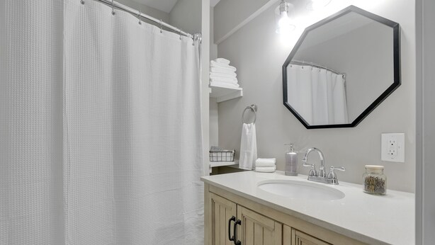 Een badkamer met douchegordijn, wastafel, spiegel en handdoekhouder.