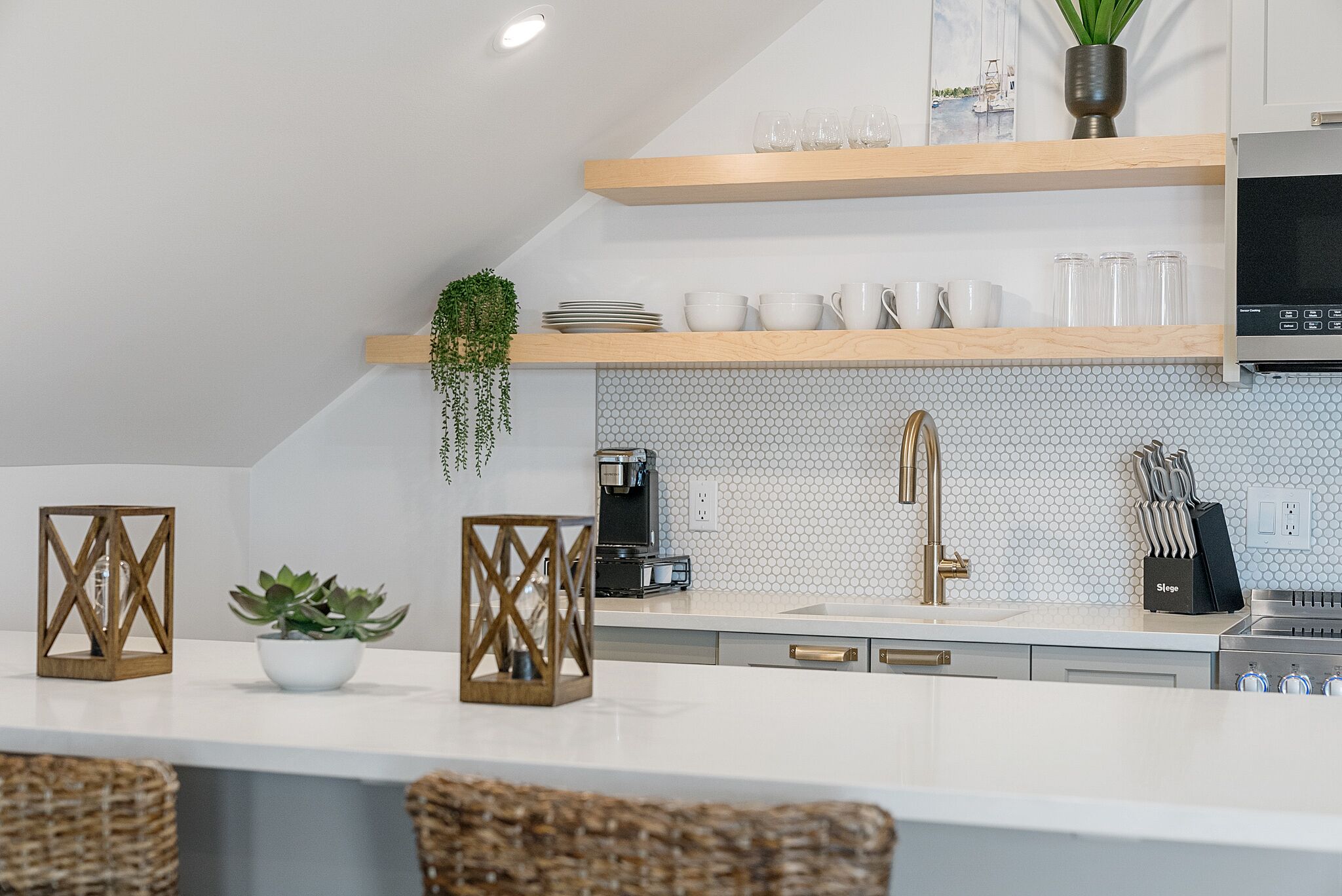 Una cocina moderna con encimeras blancas, estantes de madera y una cafetera.