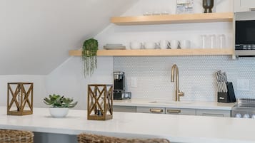 Una cocina moderna con encimeras blancas, estantes de madera y una cafetera.
