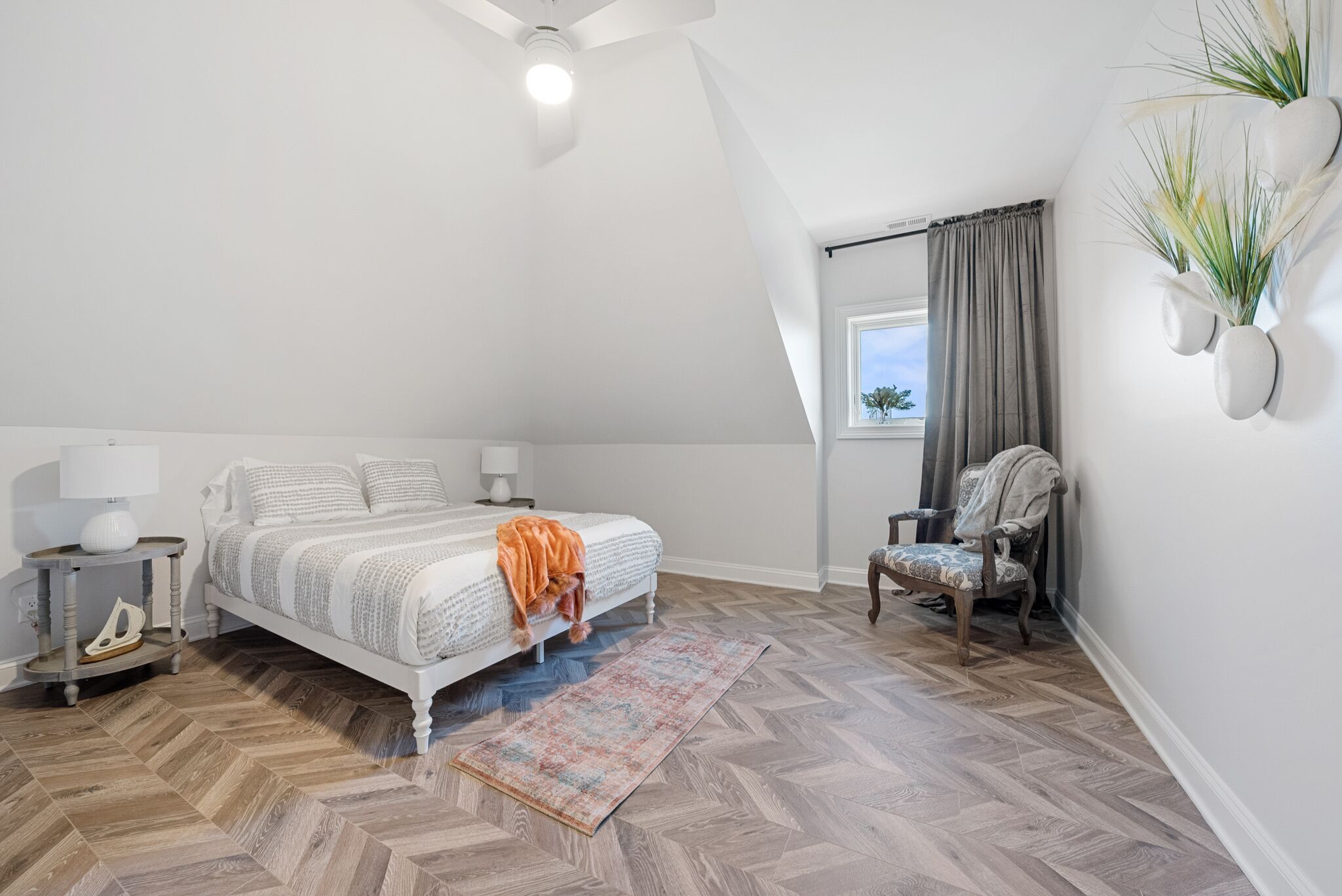 Un dormitorio con cama, mesita de noche, silla y ventana con cortinas.
