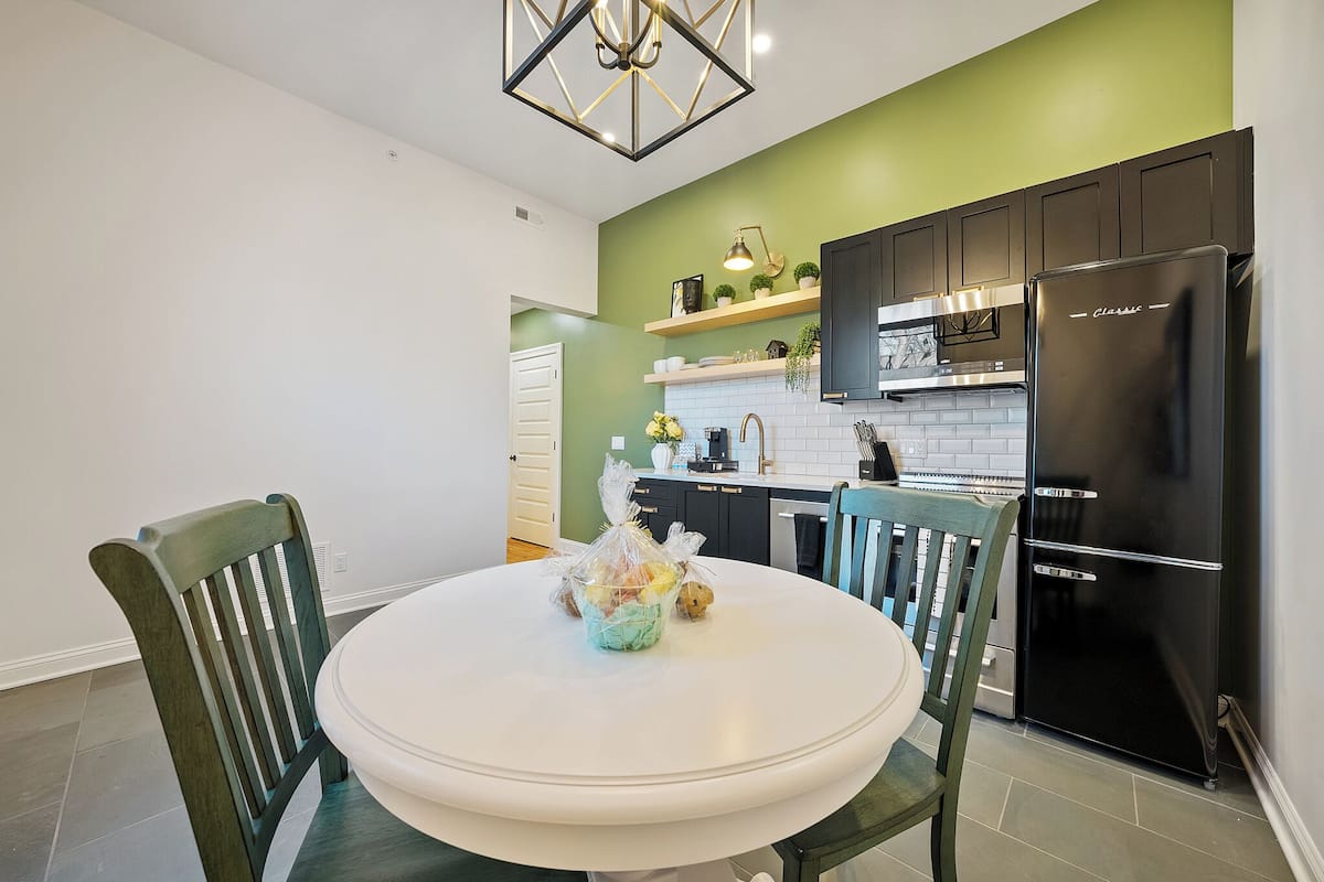Una cocina con una mesa blanca, sillas verdes, un refrigerador negro y una pared de acento verde.