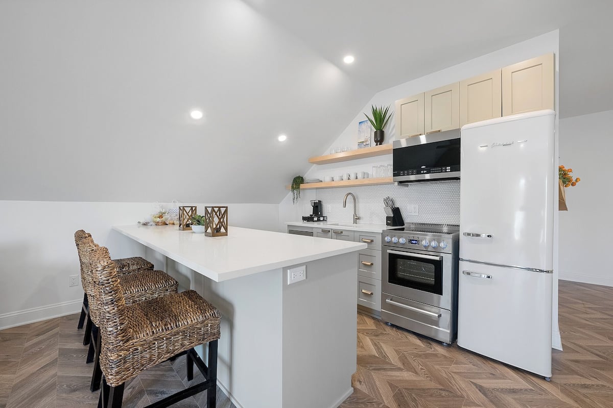 Una cocina moderna con una isla central, electrodomésticos integrados y taburetes de mimbre.