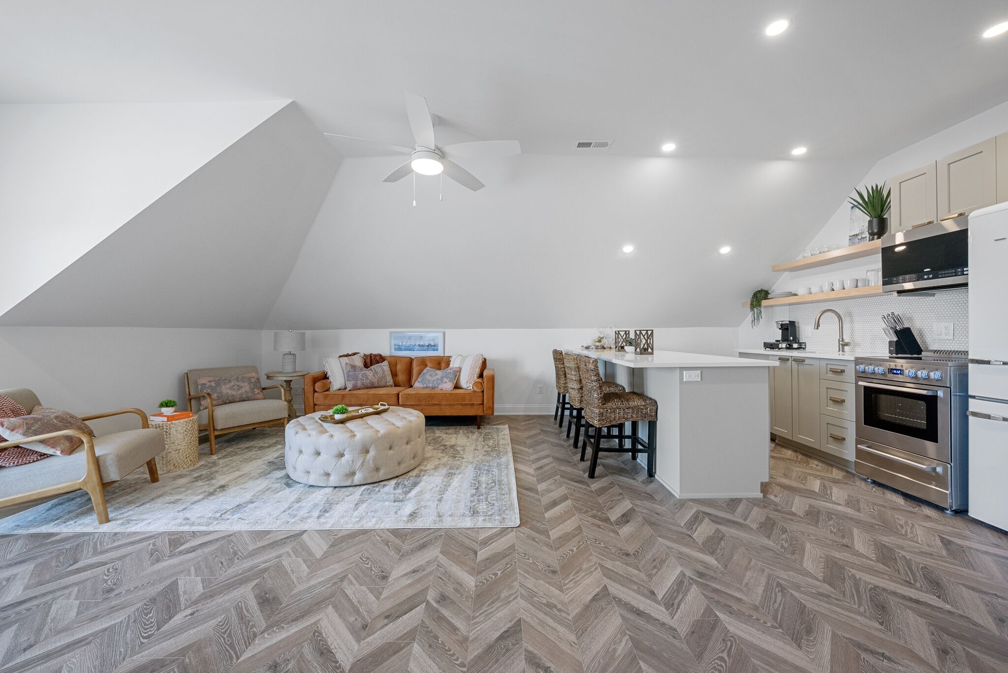 A loft-style living space with a kitchen, a sofa, a dining area, and a ceiling fan.