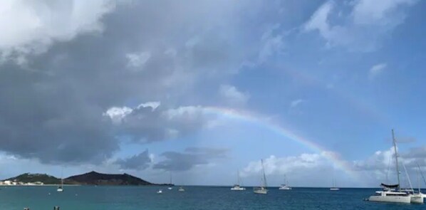 A coastal scene with a rainbow, boats, and a distant island. - Heart of Melane Villa (Grand Case)