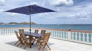 An outdoor patio with a table and chairs, a large umbrella, and a view of the sea with boats. - Heart of Melane Villa (Grand Case)