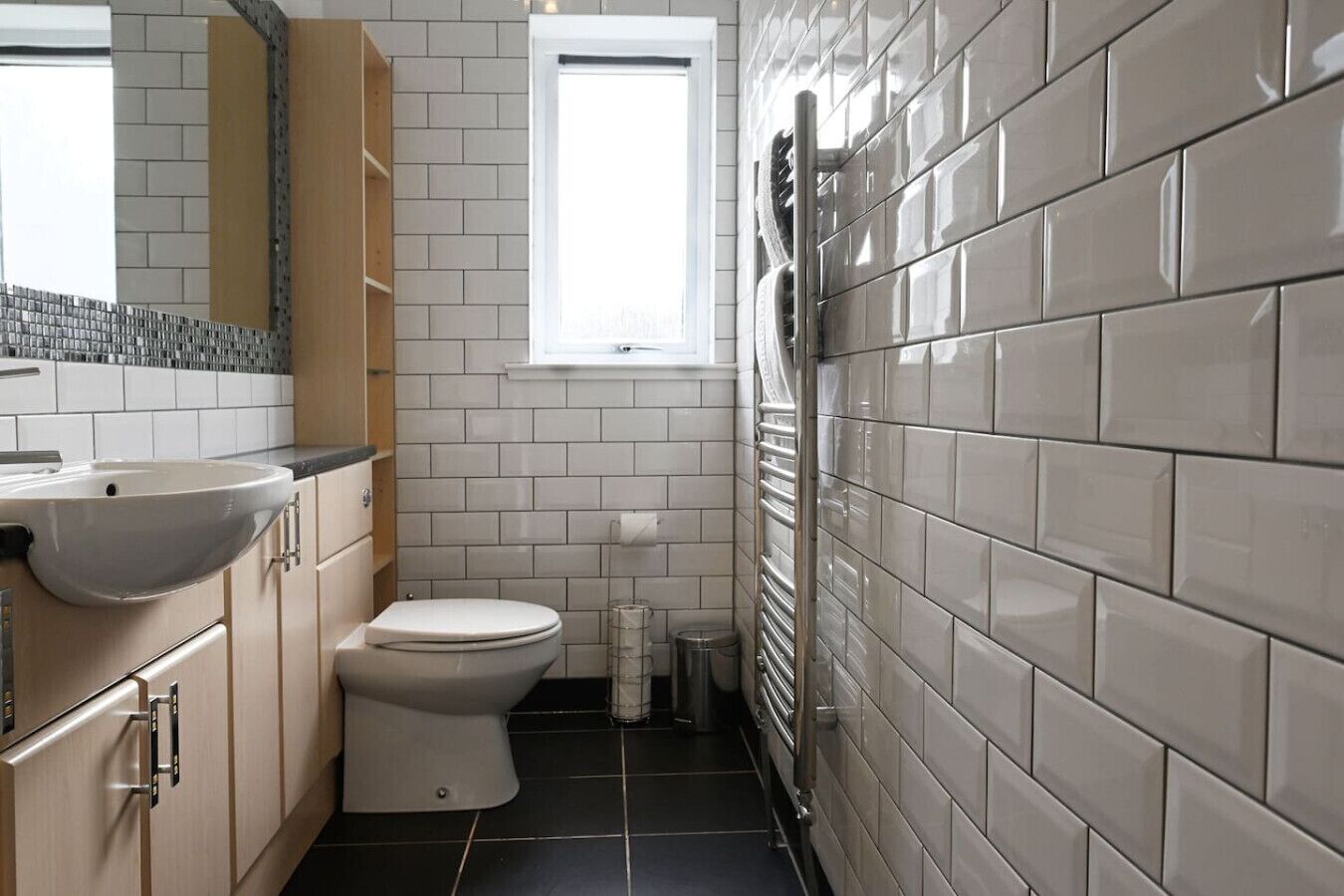 A modern bathroom with a white sink, toilet, and vanity. It features a tiled backsplash and a window providing natural light.