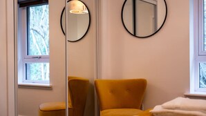 A bedroom with a bed, a chair, a mirror, and a window.