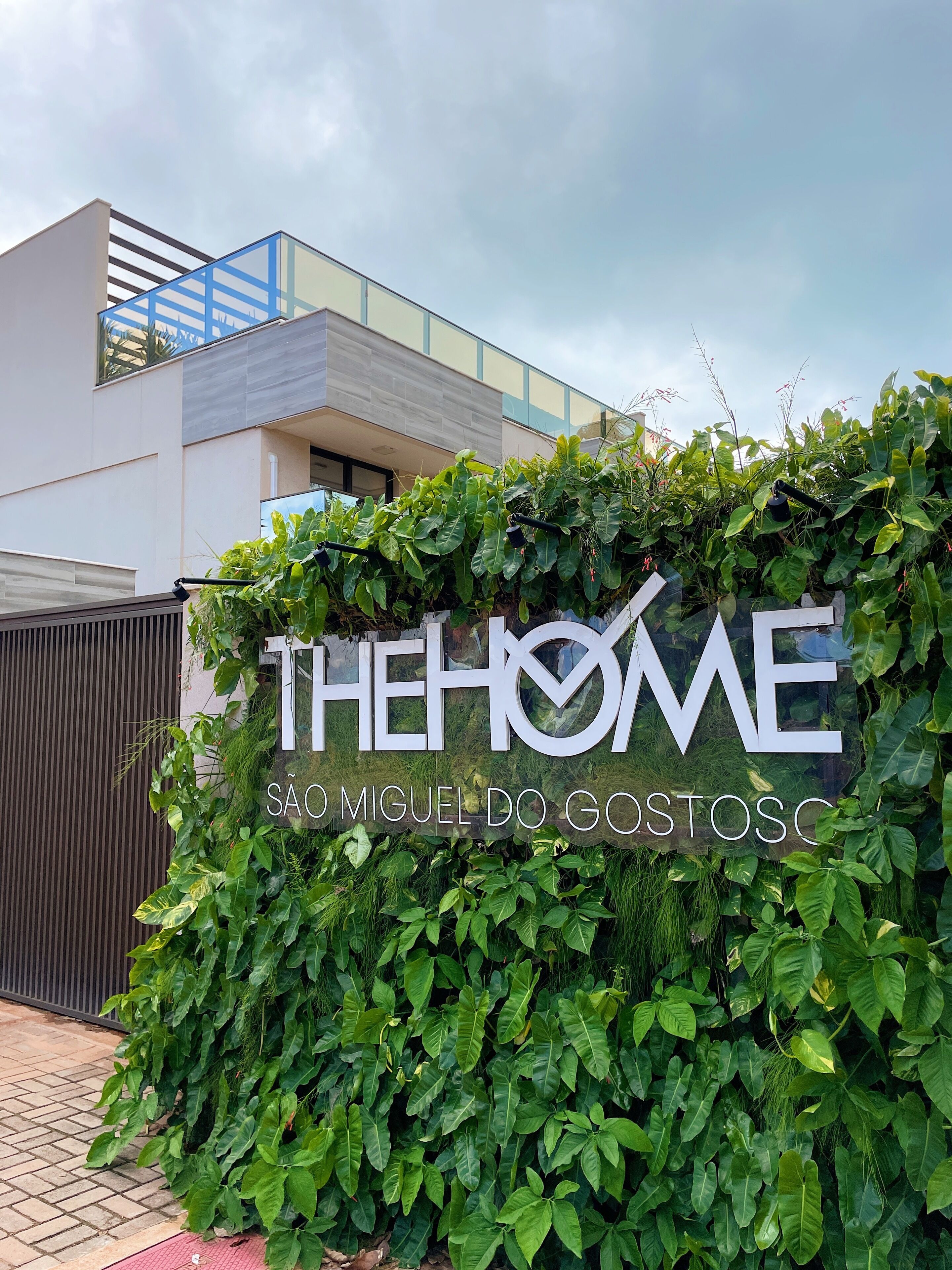 Placa com a inscrição 'THE HOME' e um conjunto de sebe verde exuberante na frente.