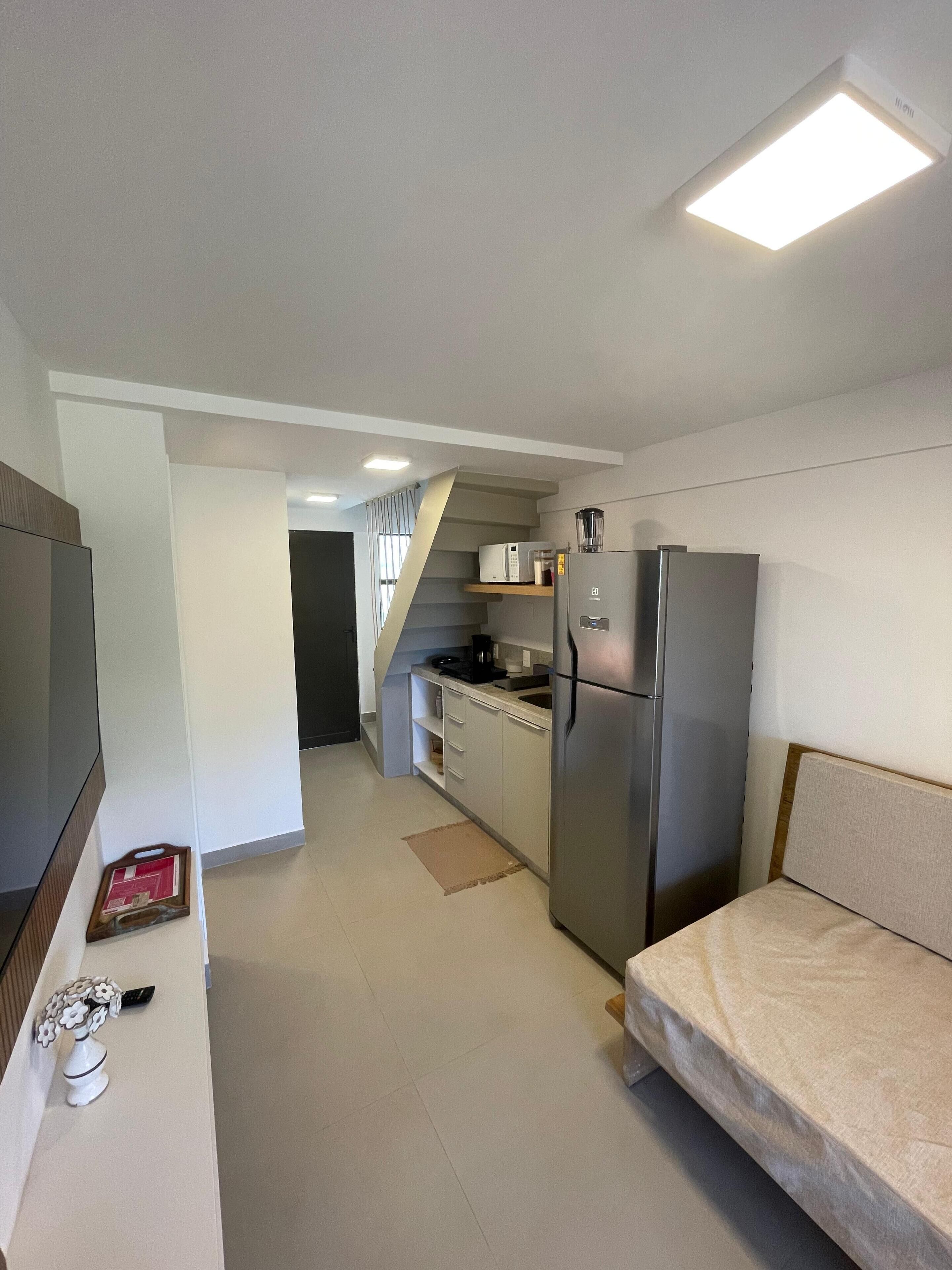 Cocina compacta con refrigerador, microondas y cafetera. Cuenta con un pequeño comedor con un banco y un jarrón decorativo.