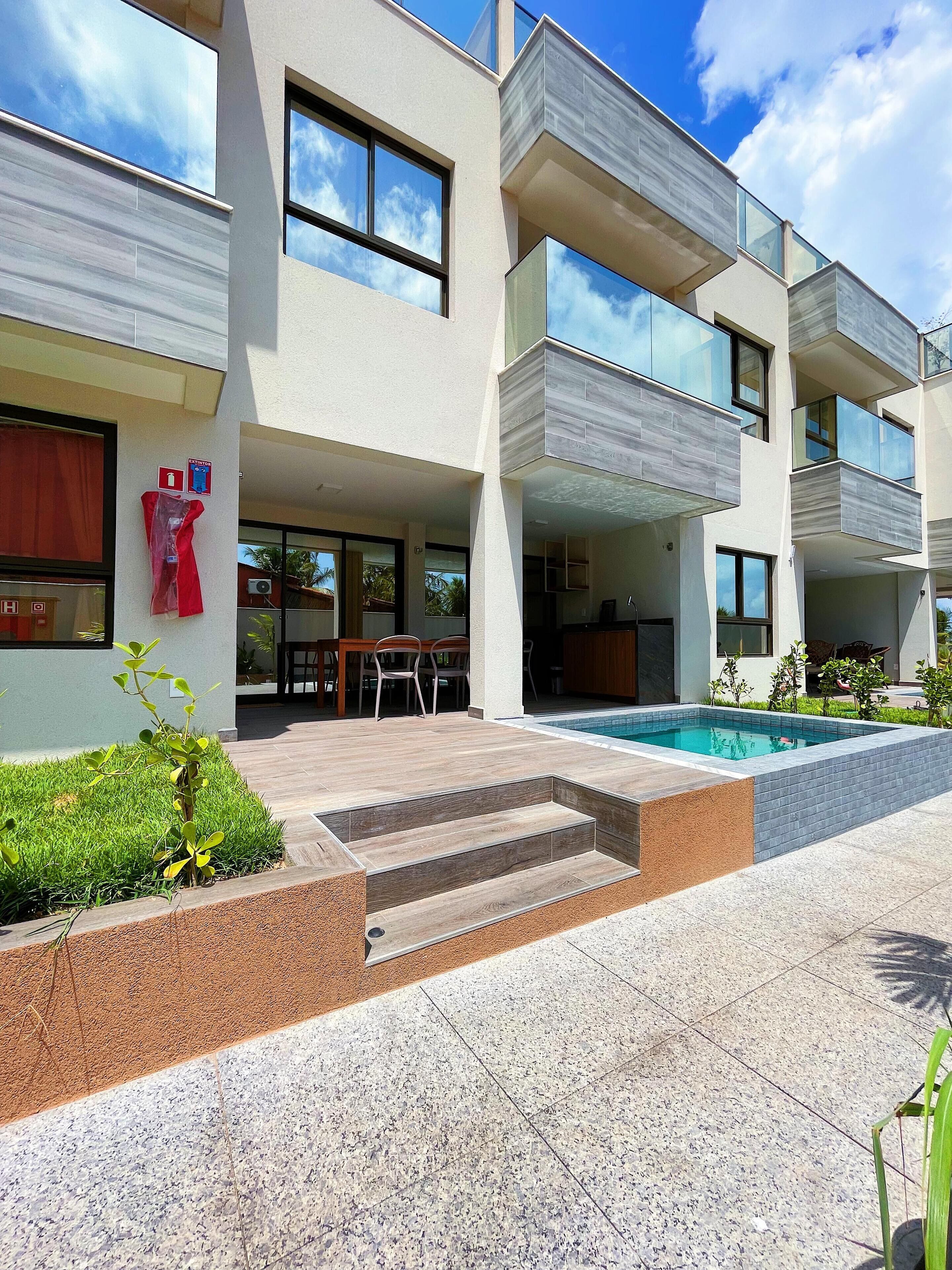 Un edificio moderno de varios pisos con piscina, mobiliario exterior y una escalera que conduce a la entrada.