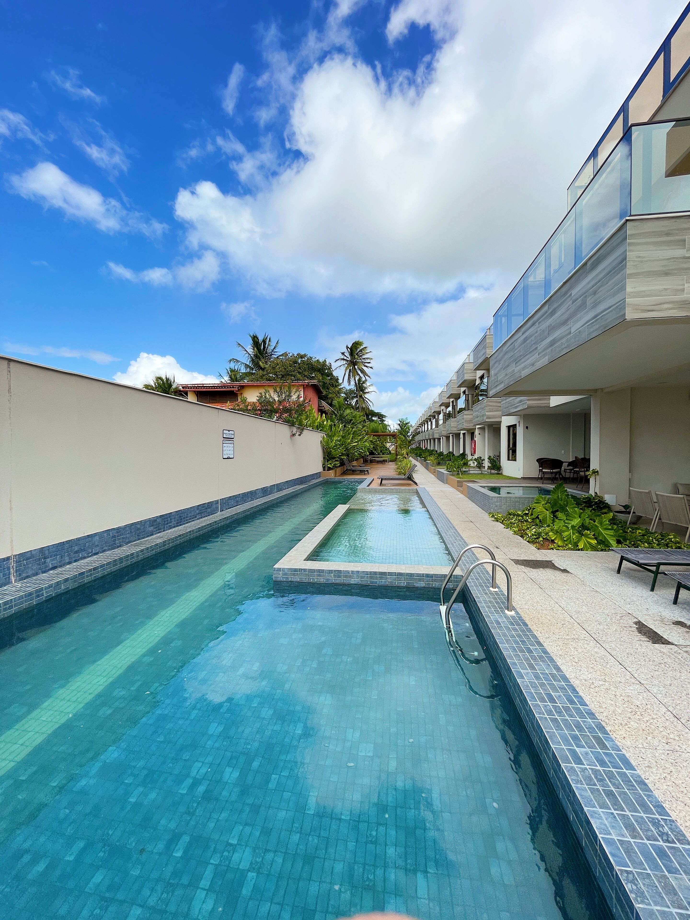 A swimming pool with clear blue water, surrounded by a tiled deck and a building with a modern design.