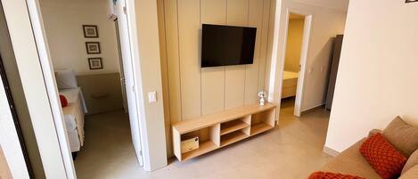 A modern living room with a flat-screen TV mounted on a wooden wall, a wooden entertainment unit, and a beige sofa with orange cushions.