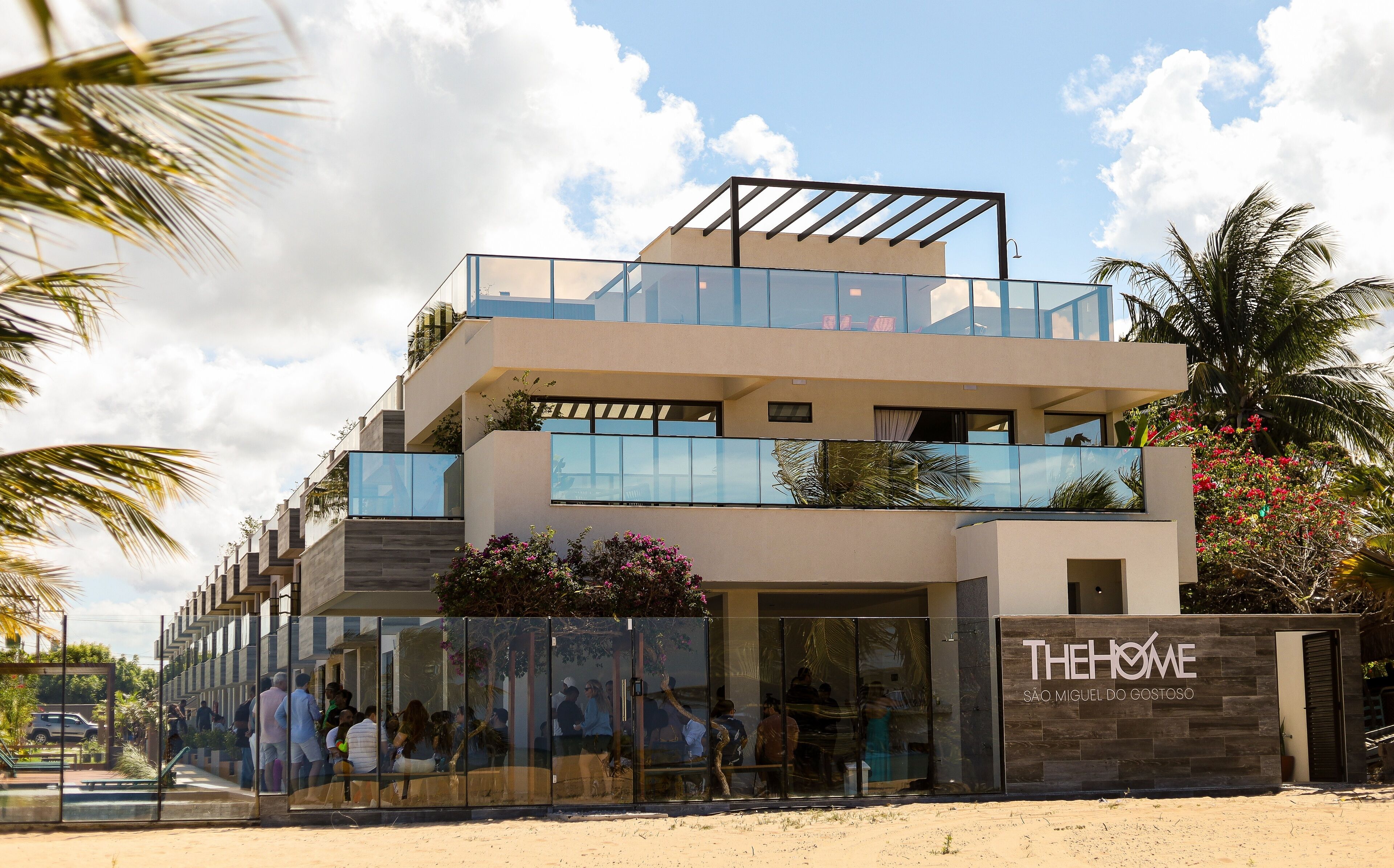 A modern two-story building with glass balconies and a sign reading "THE HOME São Miguel do Goso".