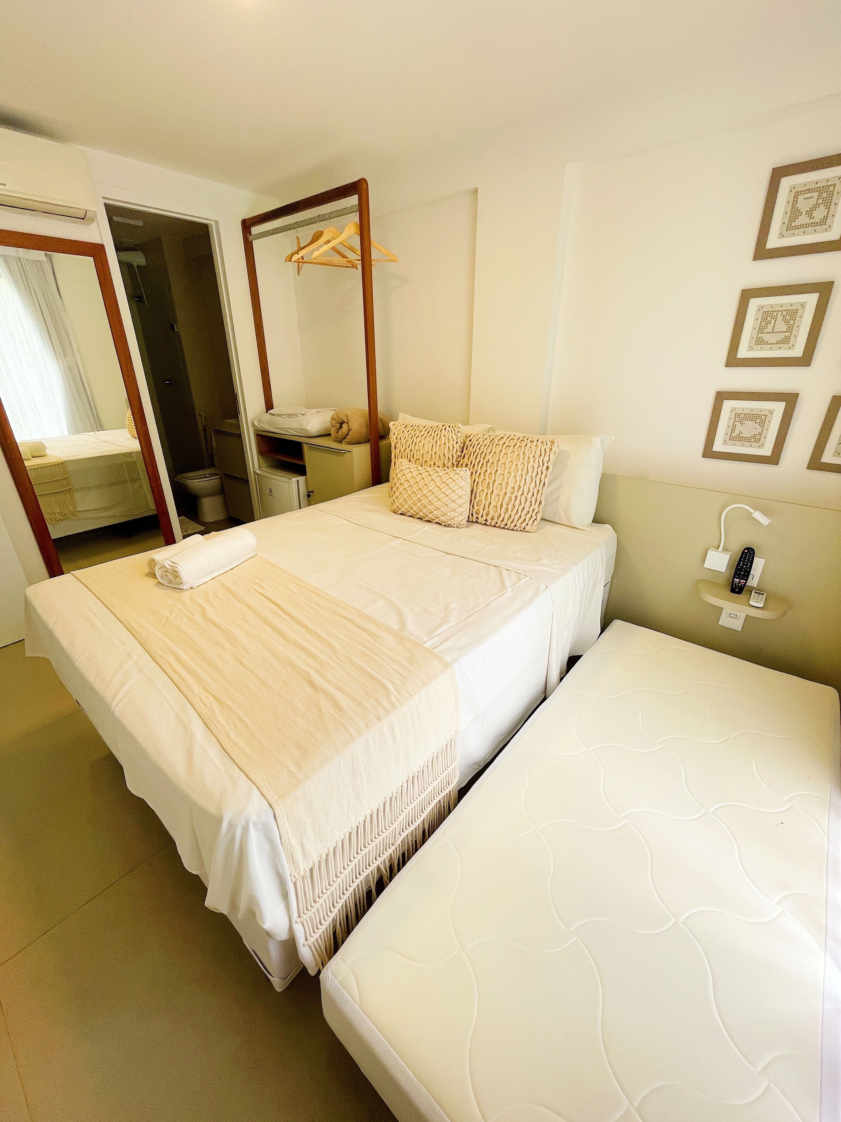 A double bed with a white comforter and pillows, a bedside table with a lamp, and a mirror on the wall.