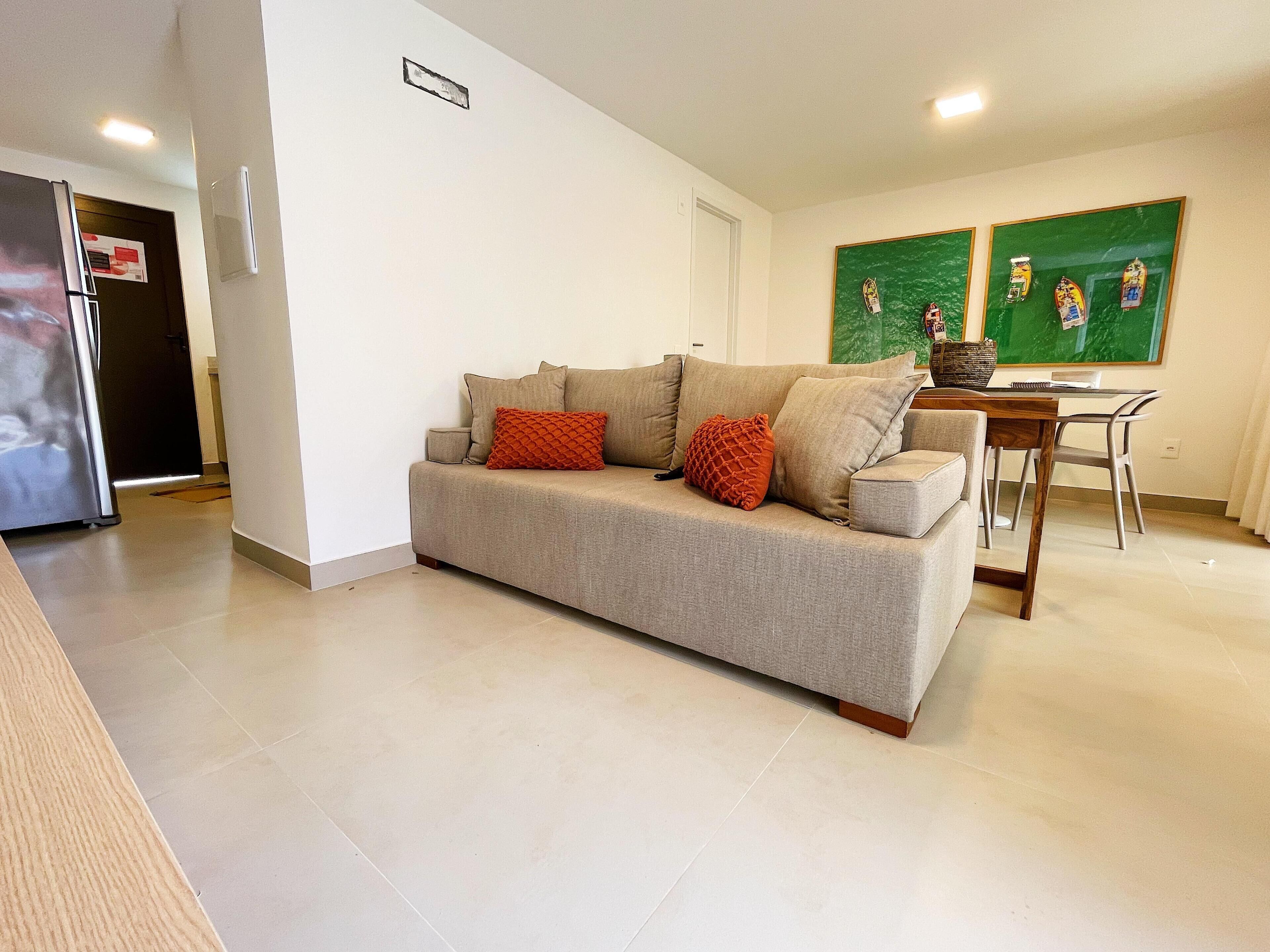 A living room with a beige sofa, a wooden dining table, and a green-framed artwork on the wall.