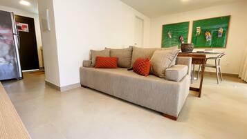 A living room with a beige sofa, a wooden dining table, and a green-framed artwork on the wall.