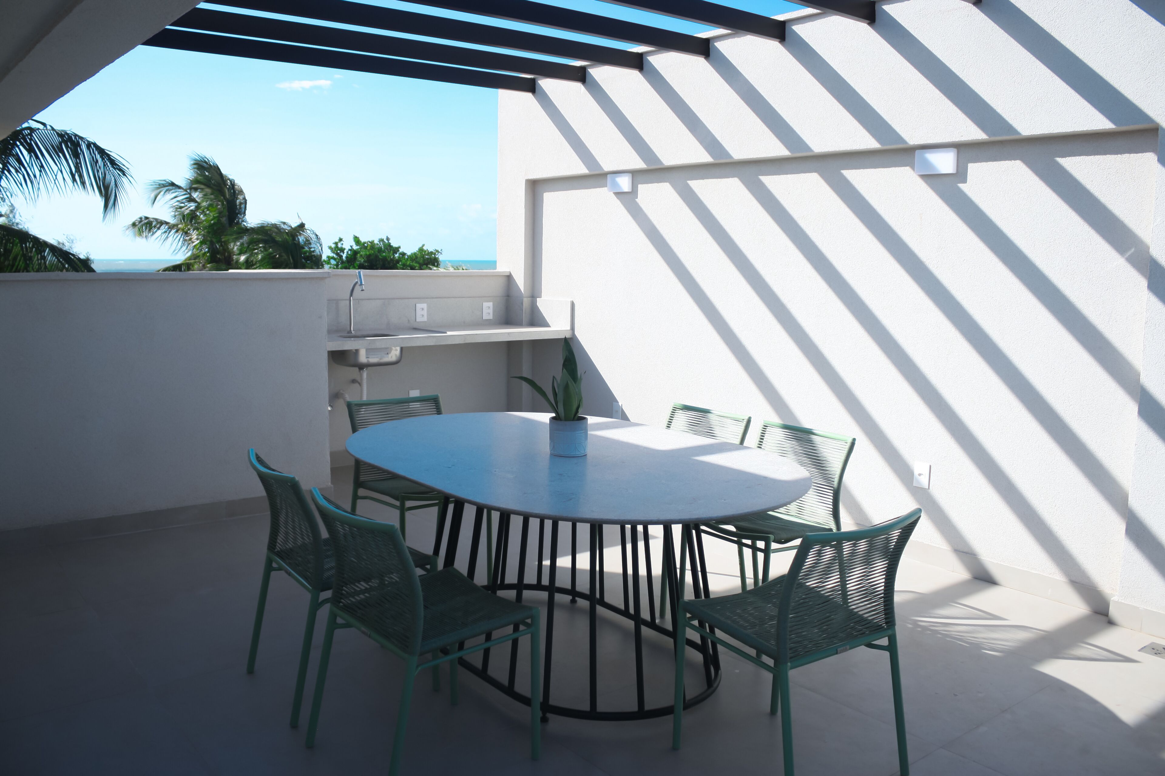 A round table with six chairs, a potted plant, and a view of the ocean.