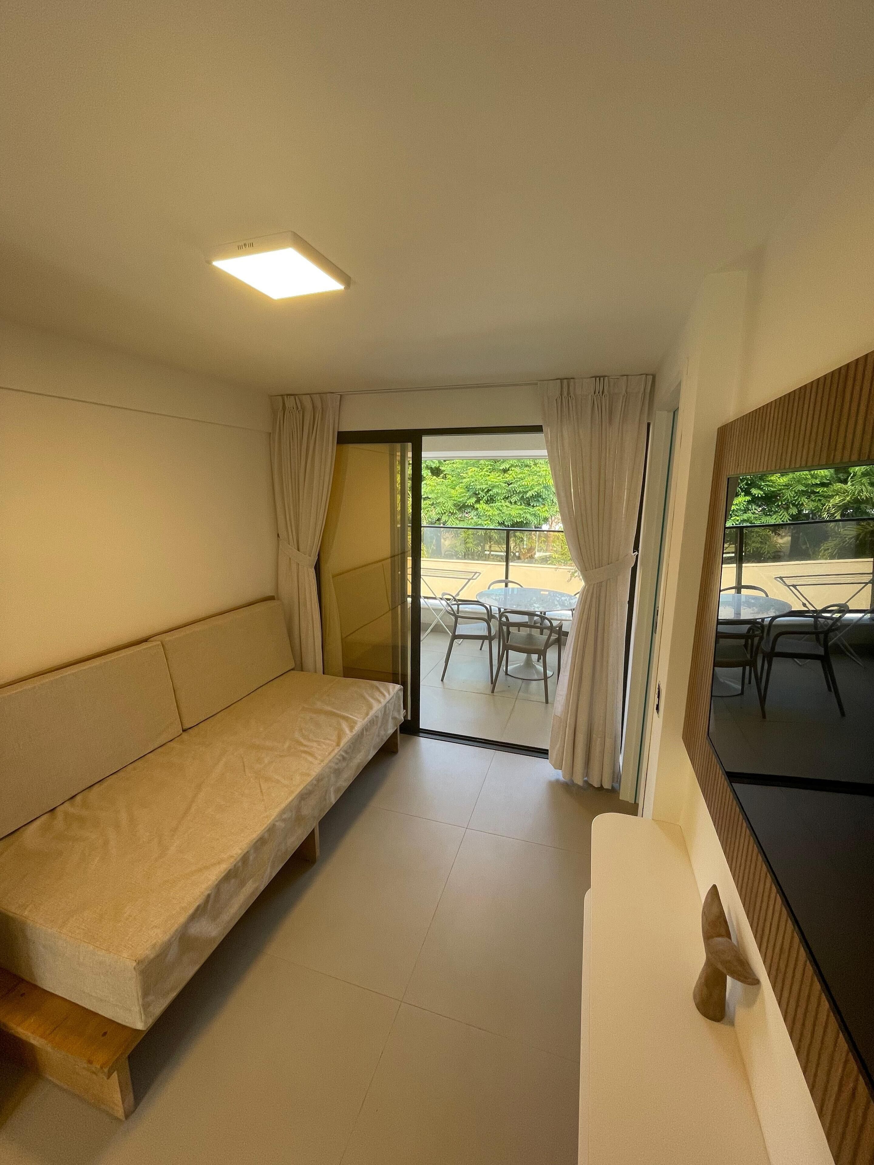 A room with a sofa bed, a TV, and a sliding glass door leading to an outdoor area with a table and chairs.