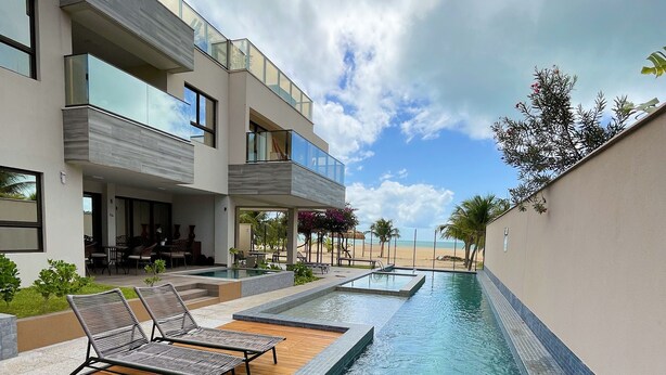 A modern hotel with a swimming pool, lounge chairs, and a view of the beach.